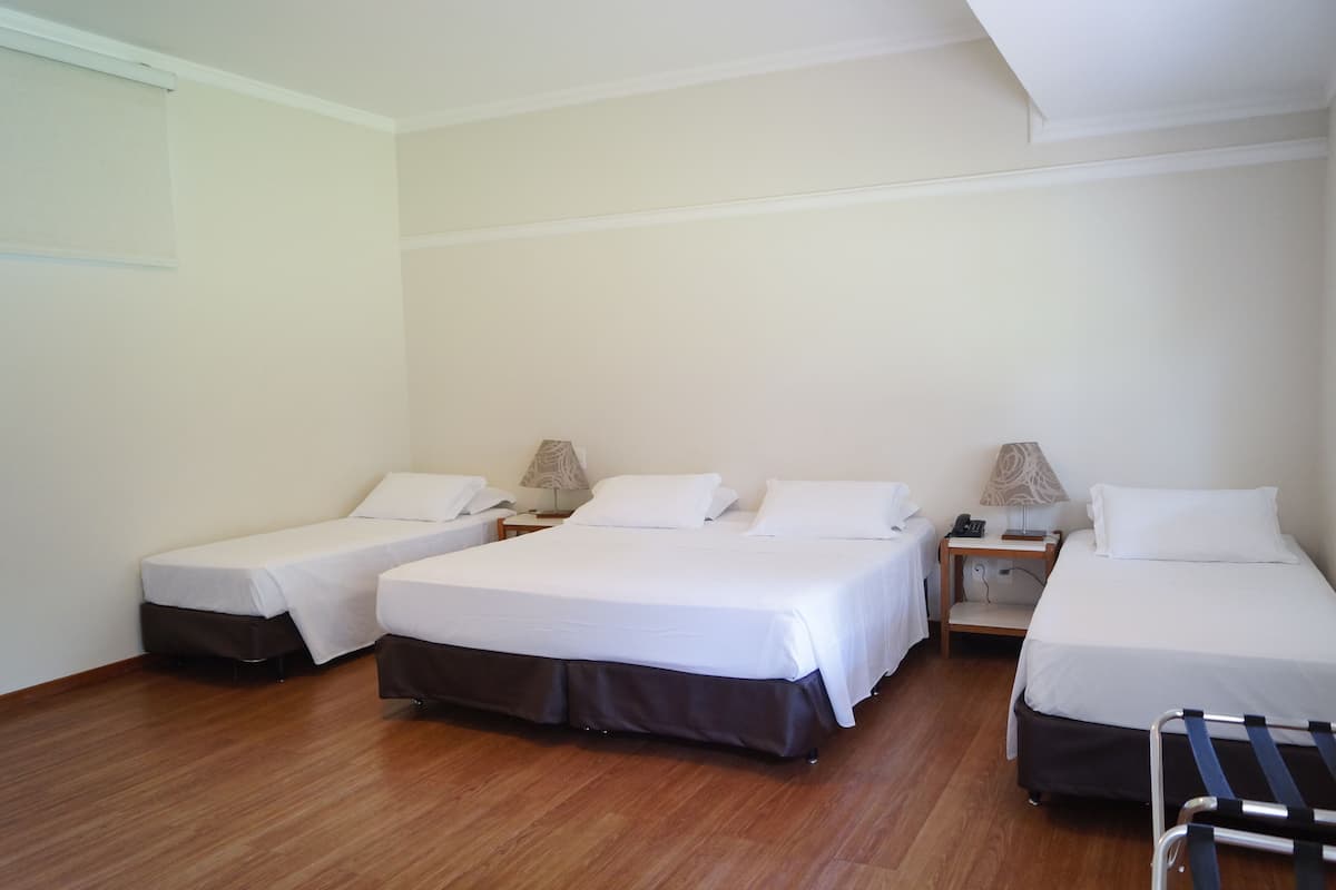 Habitación de hotel con tres camas, suelo de madera y mesitas de noche con lámparas.