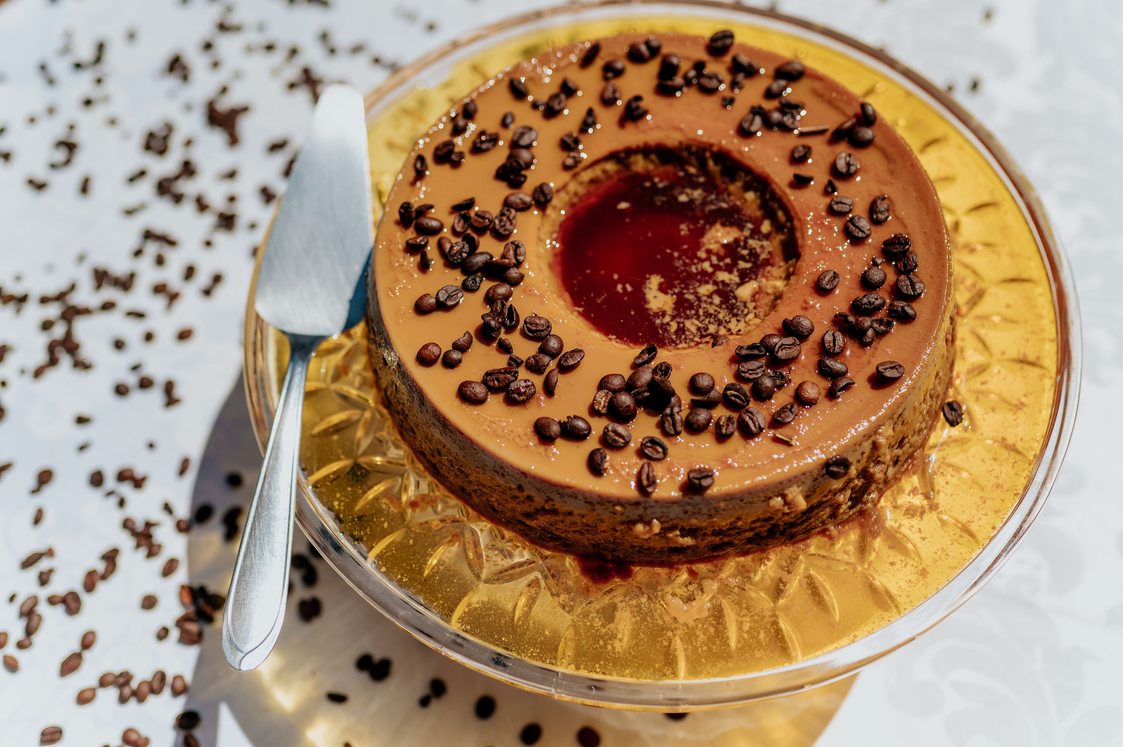 Un postre redondo con granos de café encima, servido en un plato dorado con una cuchara.