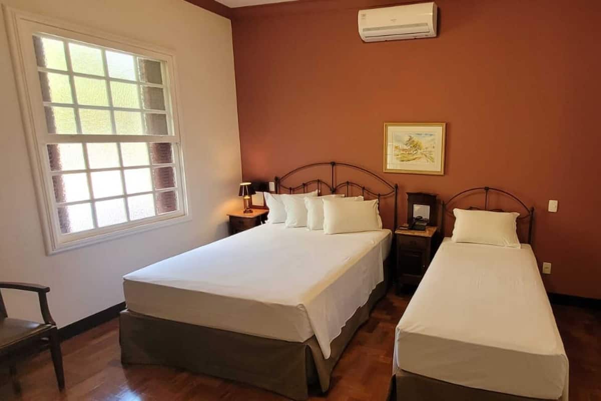 Un dormitorio con dos camas individuales, una ventana, aire acondicionado y una puerta con diseño decorativo.