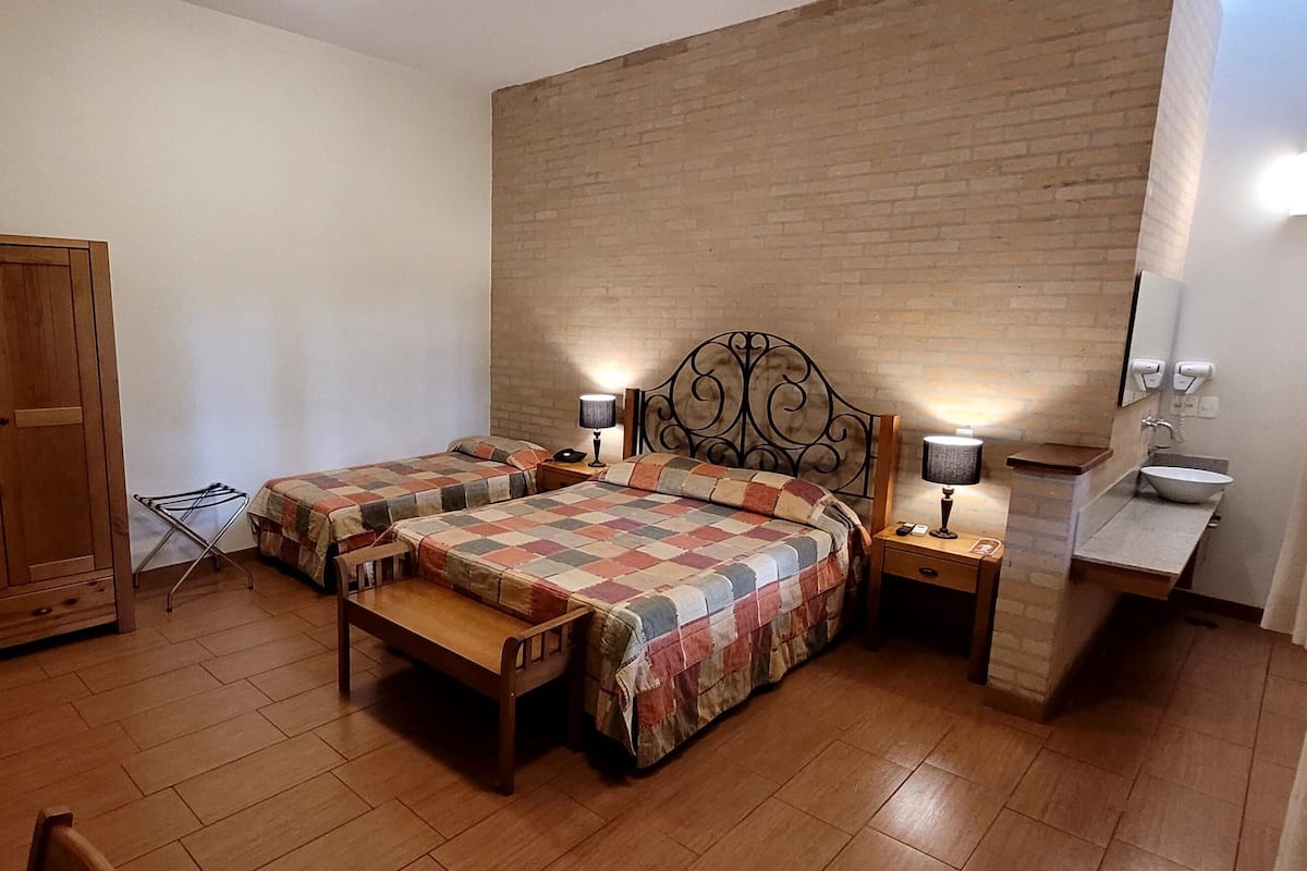 Un dormitorio con dos camas, un armario de madera, una mesita de noche con lámpara y un escritorio pequeño con espejo.