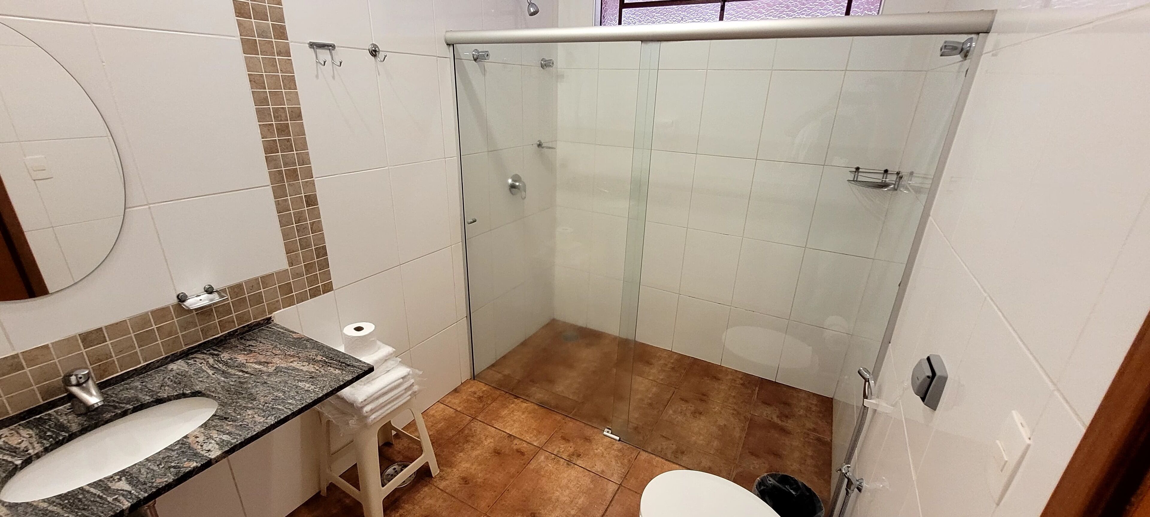 Um banheiro com chuveiro em box de vidro, pia com bancada de mármore e vaso sanitário.