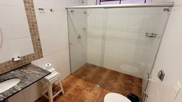 Um banheiro com chuveiro em box de vidro, pia com bancada de mármore e vaso sanitário.