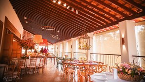 An indoor dining area with wooden tables and chairs, a ceiling with wooden beams, and hanging light fixtures.