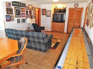 A living room with a sofa, a dining table, a shuffleboard table, and a kitchen area with a microwave. - Oceanfront 6BR, 5BA Corolla retreat with beach access, hot tub, and pool. WH-39 (Corolla)