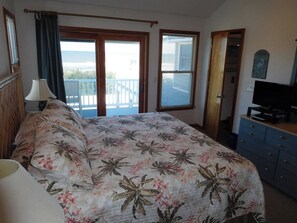 A bedroom with a bed, a dresser, a television, and a balcony door. - Oceanfront 6BR, 5BA Corolla retreat with beach access, hot tub, and pool. WH-39 (Corolla)