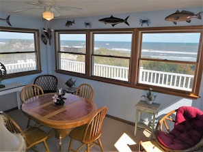 Un comedor con mesa y sillas, ventanas amplias con vista al océano, y decoración de peces y cangrejos en la pared.