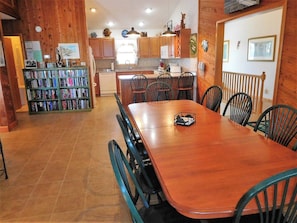 A wooden interior with a dining table, chairs, a bookshelf, and a kitchen area. - Oceanfront 6BR, 5BA Corolla retreat with beach access, hot tub, and pool. WH-39 (Corolla)