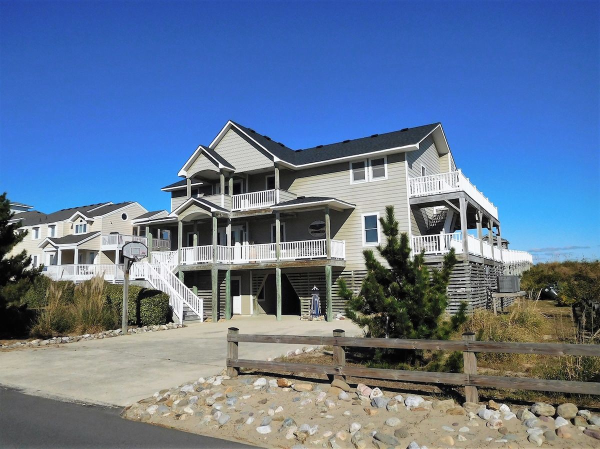 A multi-story beachfront property with balconies, a covered porch, and a clear view of the ocean.