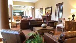 A spacious living area with leather sofas, a wooden coffee table, and a large vase. There is a dining area in the background with a wooden cabinet and a chair.