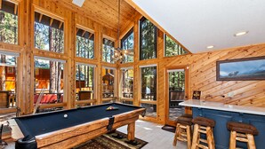 Ein Holzinterieur mit Billardtisch, Barhocker und Küchenzeile.