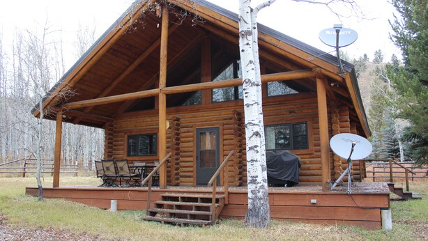 Une cabane en rondins avec un porche, une antenne parabolique et un espace extérieur aménagé avec des sièges.