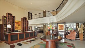 A spacious lobby with a reception desk, a large round table, and a staircase leading to an upper level.