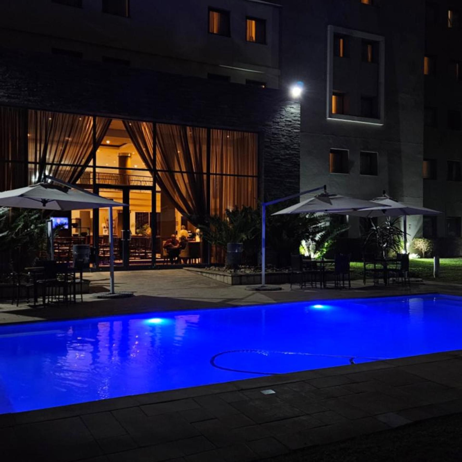 Una piscina con sombrillas, un restaurante con terraza y un edificio con varias ventanas.