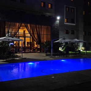 Una piscina con ombrelloni, un ristorante con tavoli all'aperto e un edificio con numerose finestre.