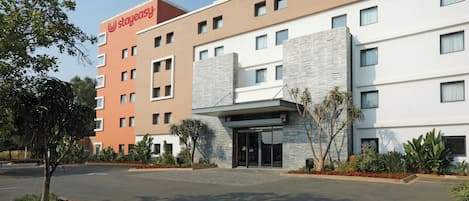 A multi-story hotel with a modern facade, a prominent brand logo, and a landscaped entrance.