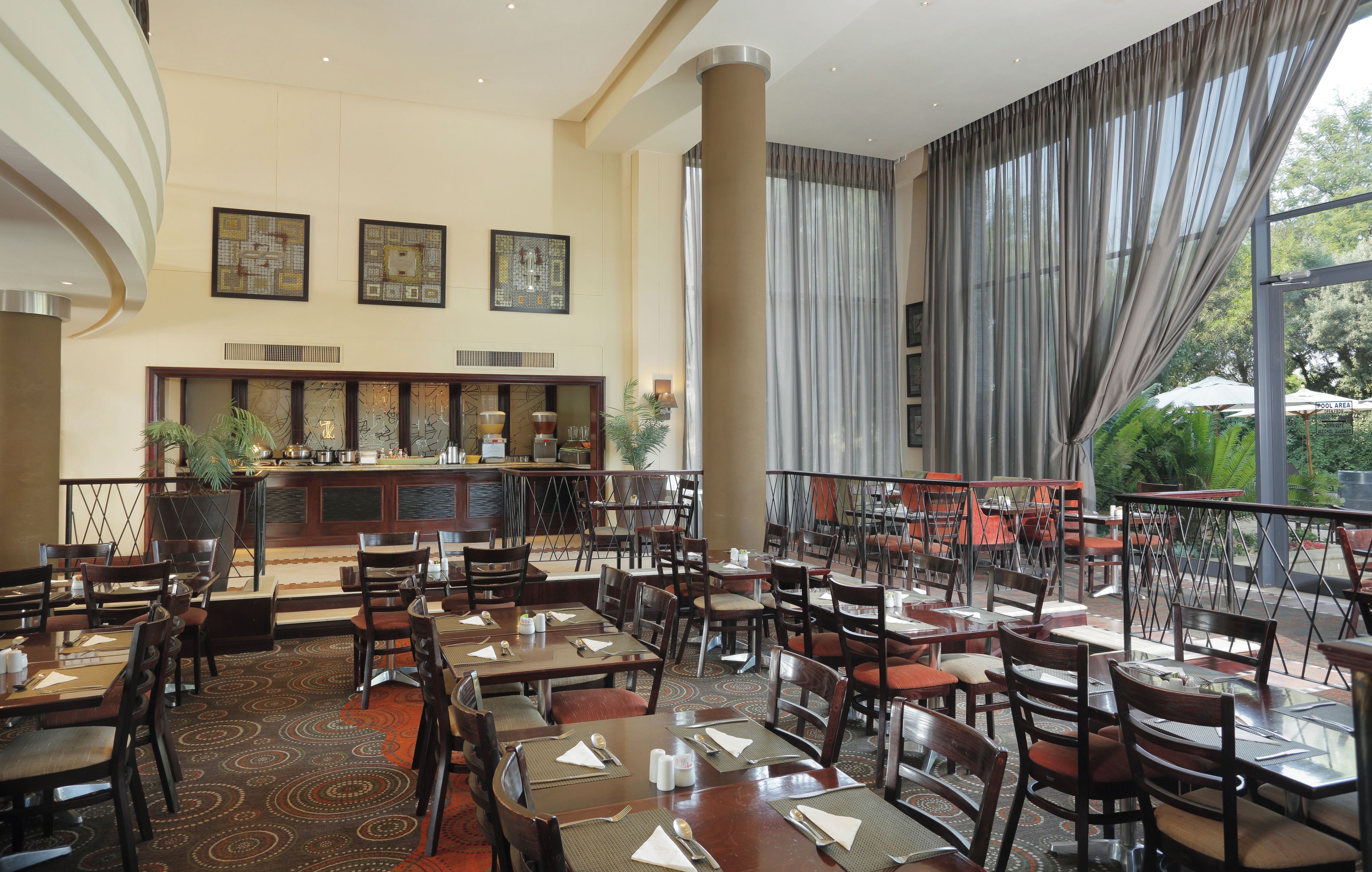 Een ruim restaurant met meerdere tafels en stoelen, een bar en grote ramen met uitzicht op het omliggende landschap.