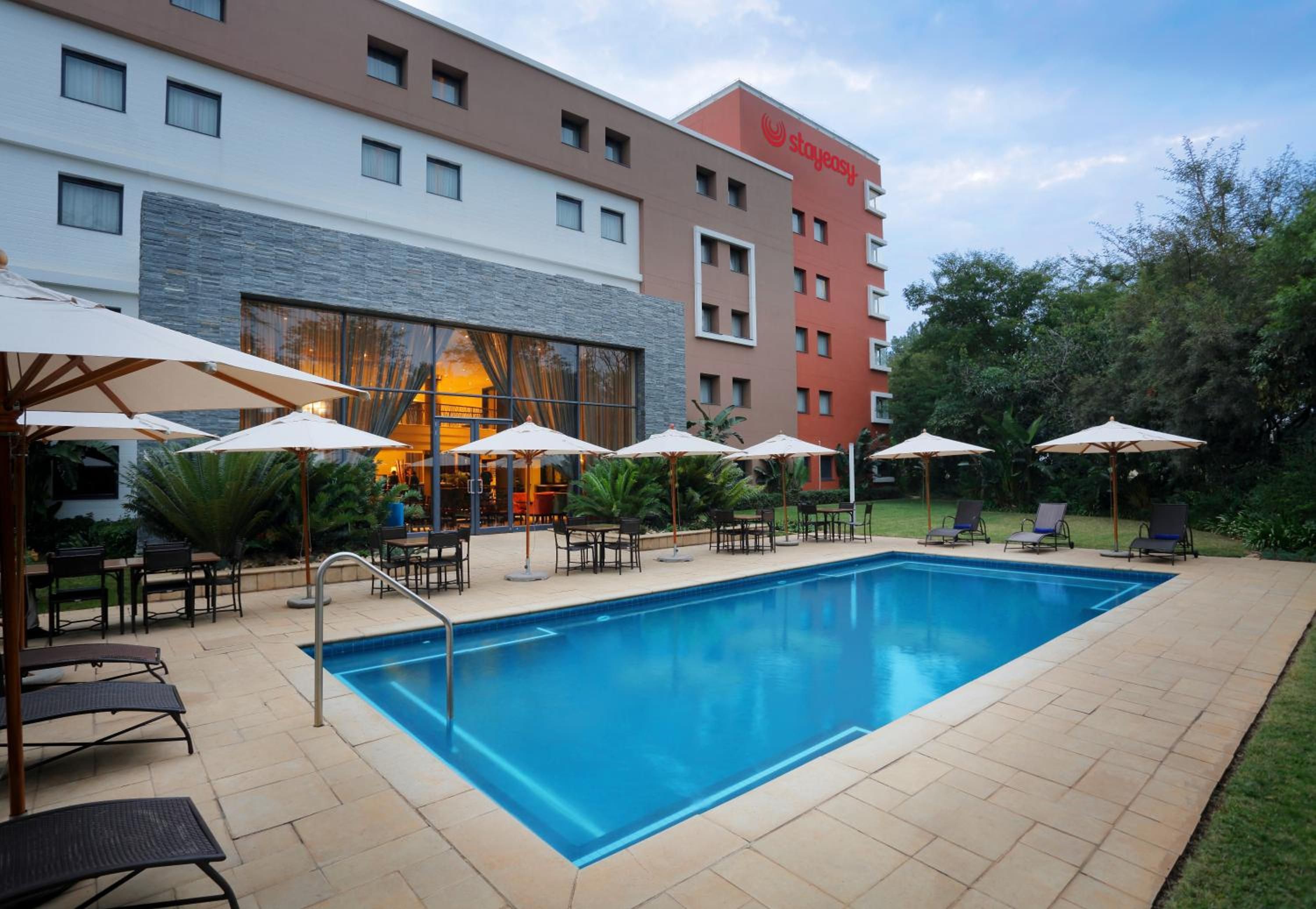 A hotel pool area with a rectangular pool, lounge chairs, and umbrellas.