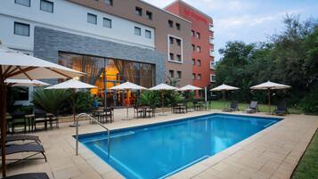 Ein Hotelpoolbereich mit rechteckigem Pool, Liegestühlen und Sonnenschirmen.