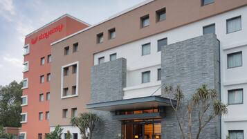 A multi-story hotel with a StayEasy sign, a parking lot, and a landscaped entrance area.