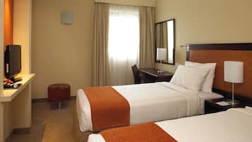 A hotel room with two beds, a desk with a computer, a chair, a TV, and a window with curtains.