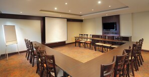 A conference room with a long table, multiple chairs, a projector screen, and a flat-screen TV mounted on the wall. - Stayeasy Rustenburg (Rustenburg)