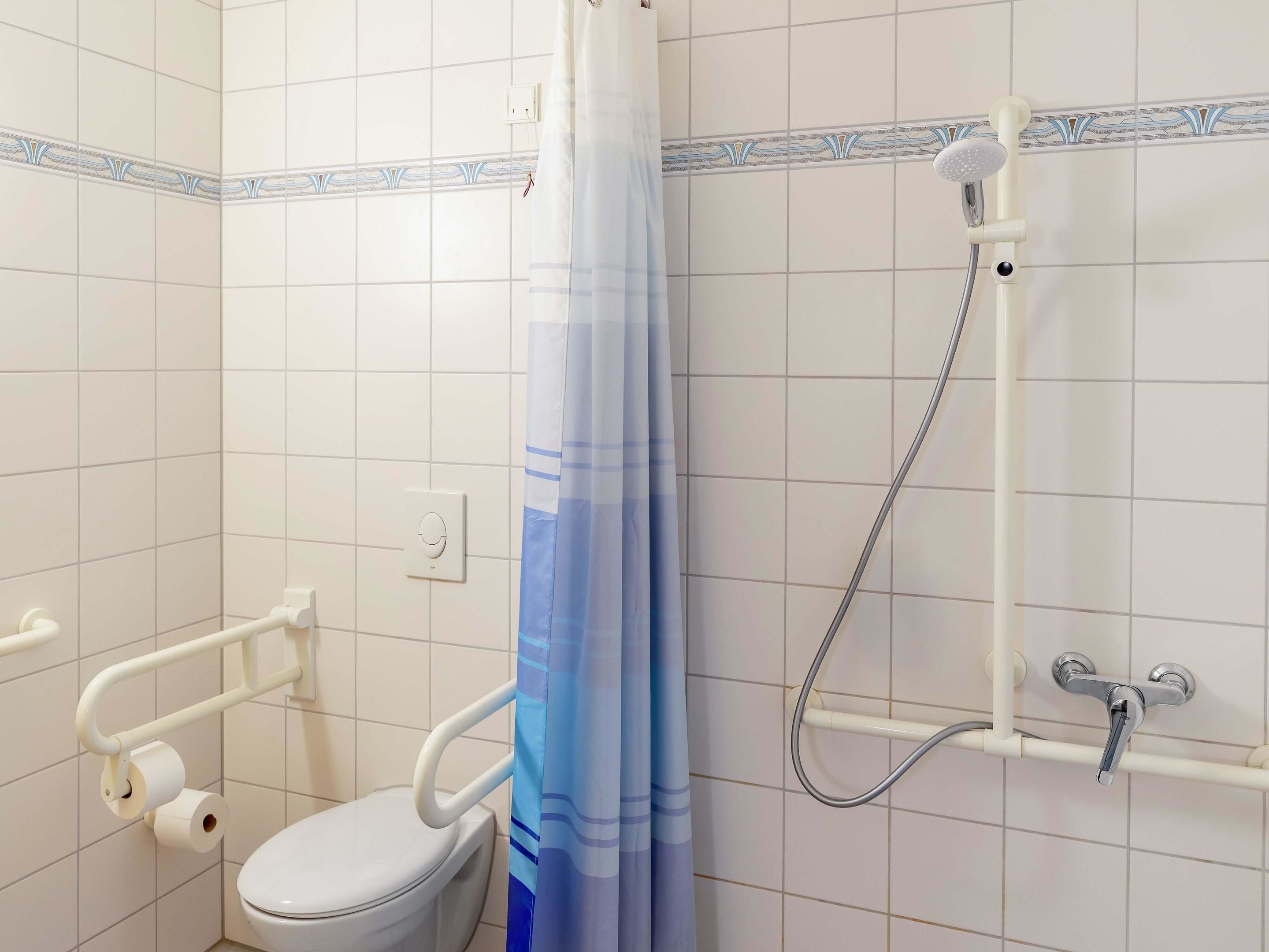 Un baño con inodoro, ducha y barra de apoyo.
