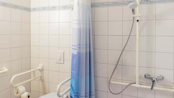Un baño con inodoro, ducha y barra de apoyo.