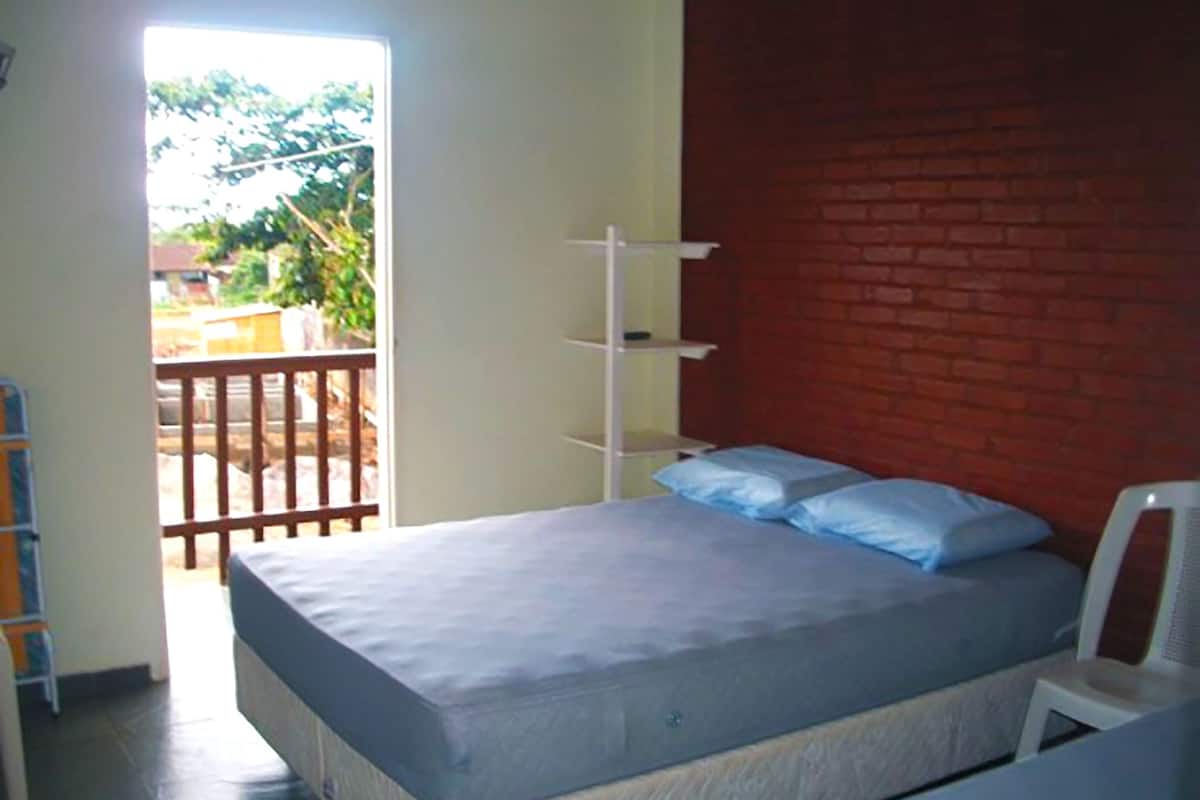 A bedroom with a bed, a white chair, a brick wall, and a balcony.
