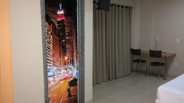 A hotel room with a bed, a desk, two chairs, a television, and a view of a city street at night.