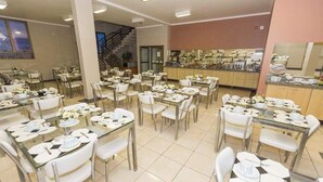 A dining area with multiple tables and chairs, a kitchen area, and a staircase.