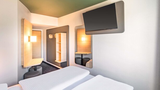 A hotel room with a bed, a TV mounted on the wall, and a mirror. - B&B HOTEL Hannover-Laatzen (Laatzen)