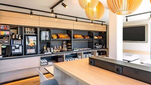 A modern kitchen with wooden cabinets, a coffee machine, and a large island with seating. - B&B HOTEL Hannover-Laatzen (Laatzen)