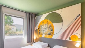 Une chambre d’hôtel avec deux lits, une grande fenêtre et une fresque murale représentant un paysage urbain.