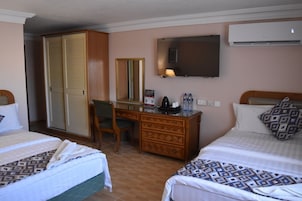 A hotel room with two beds, a desk, a wardrobe, and a TV.