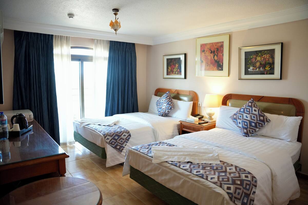 Ett hotellrum med två sängar, ett skrivbord, en stol, en lampa och konstverk på väggarna.