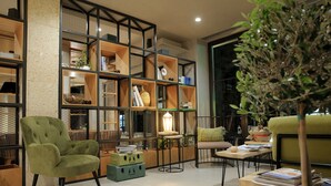 Un salón acogedor con un sillón verde, una estantería de madera y una mesita con libros y una lámpara.