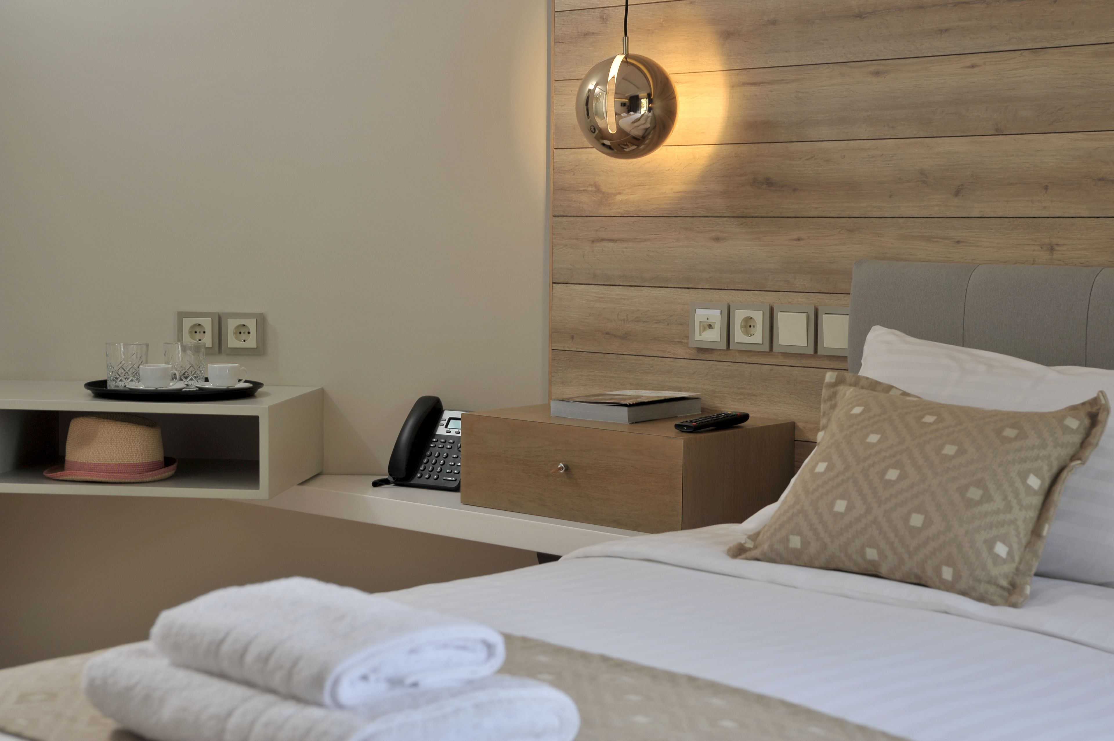 Una habitación de hotel moderna con una pared de madera, una mesita de noche con un teléfono, una lámpara y una cama con un cojín estampado.
