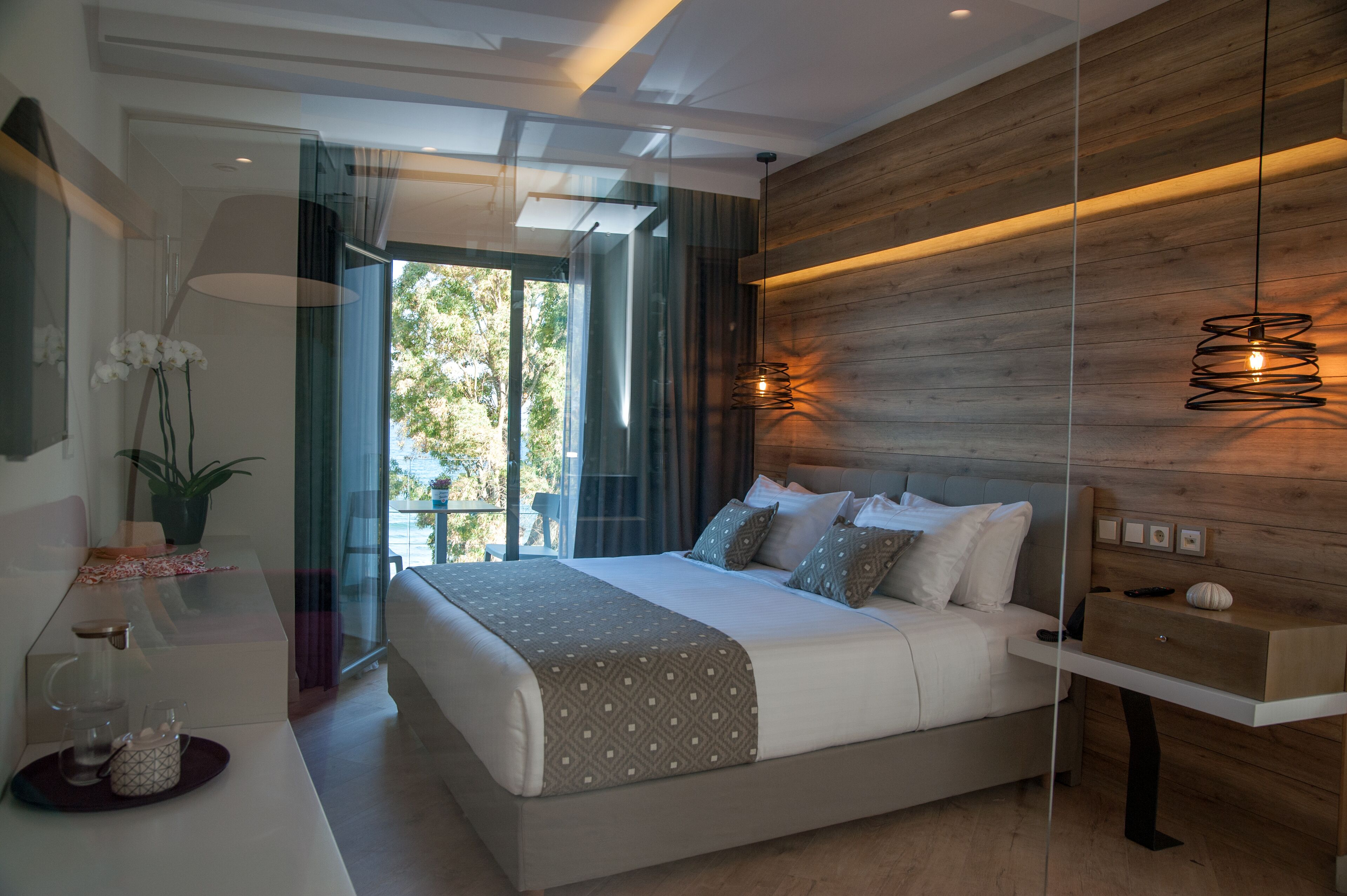 Una camera da letto moderna con un letto grande, comodini, un divisorio in vetro e una parete d'accento in legno.