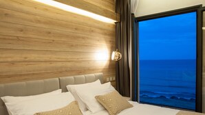 Un dormitorio con cabecera de madera, una cama con almohadas blancas y estampadas, y vista al océano a través de un ventanal grande.