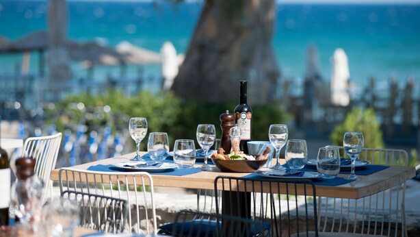 Una mesa lista para comer con vista al mar y un árbol grande al fondo.