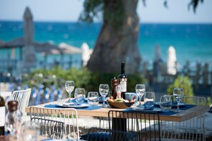 Una mesa lista para comer con vista al mar y un árbol grande al fondo.