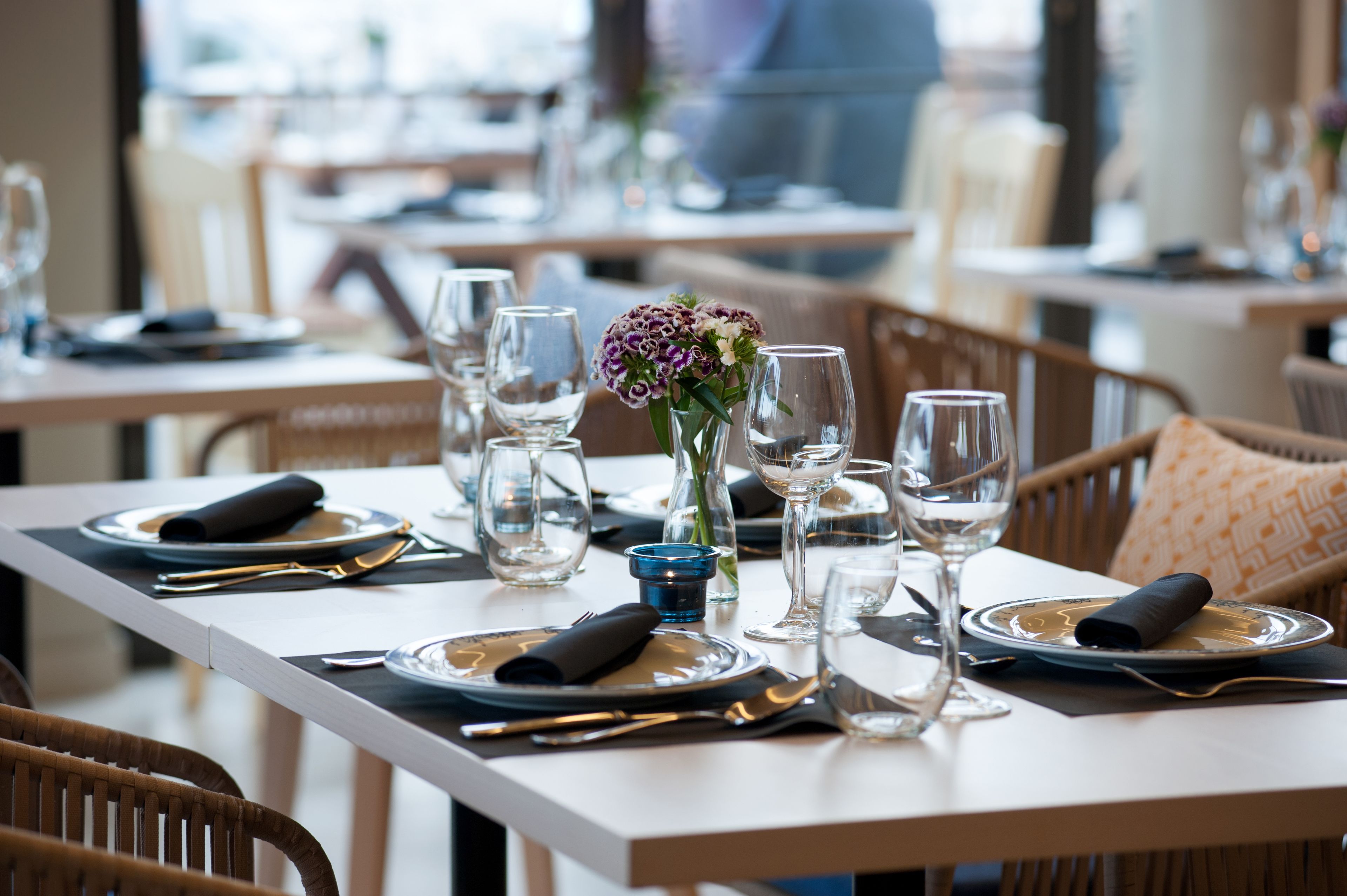 A dining table set with plates, cutlery, glasses, and a vase with flowers.