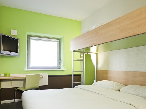 Una habitación de hotel con cama, escritorio, silla, televisor y ventana.