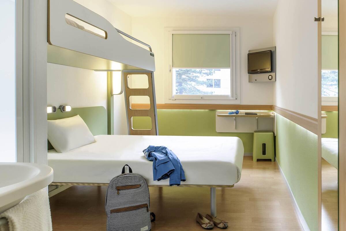Een kleine kamer met stapelbedden, een bureau en een raam.