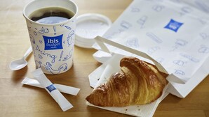 Una taza de café, un croissant y una servilleta sobre una mesa de madera.