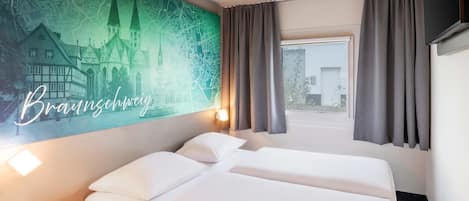 Habitación de hotel con cama, mesita de noche de madera, mapa colgado en la pared y ventana con cortinas.
