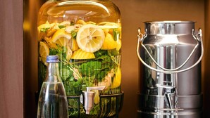 A large glass container with lemons and mint leaves, a metal pitcher, and a bottle. - B&B HOTEL Braunschweig-West (Braunschweig)
