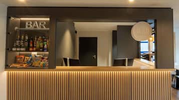 Een bar in een hotel, met een houten receptiebalie, planken vol snacks en drankjes, en een bord met de naam van het hotel.