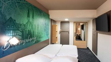A hotel room with a bed, a flat-screen TV, a mirror, and a wall with a cityscape mural.