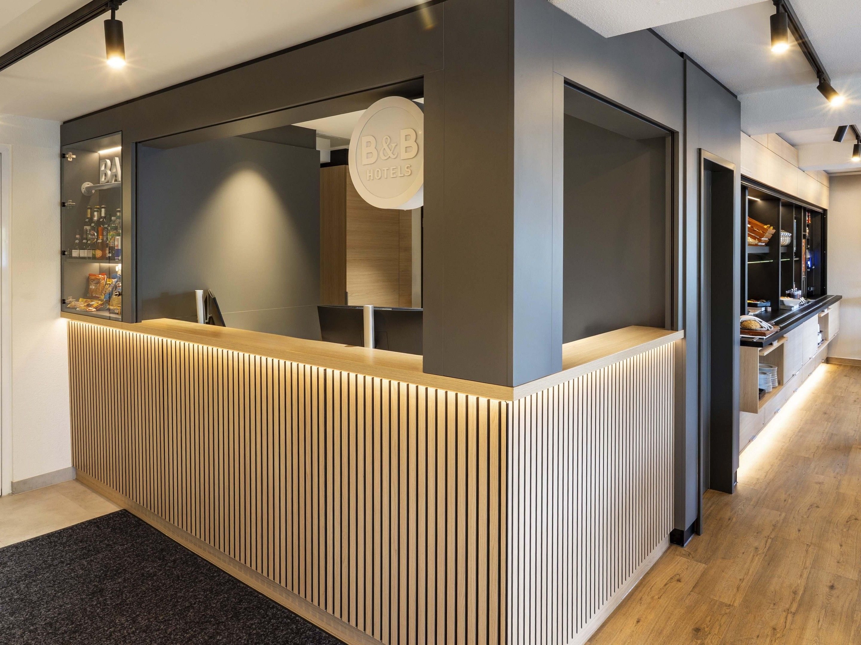 A reception desk with a modern design, featuring a wooden slatted front panel and a glass enclosure with a sign.